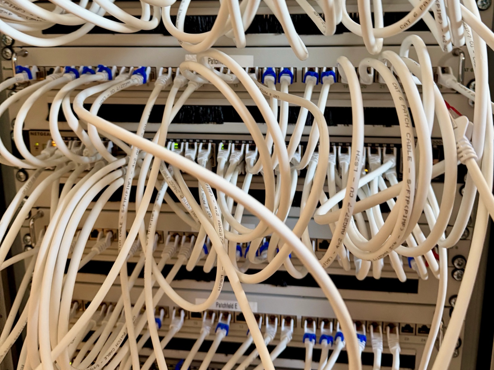 Netzwerkschrank der Praxis: dicht verlegte weiße Netzwerkkabel zwischen Patchfeldern und Switches