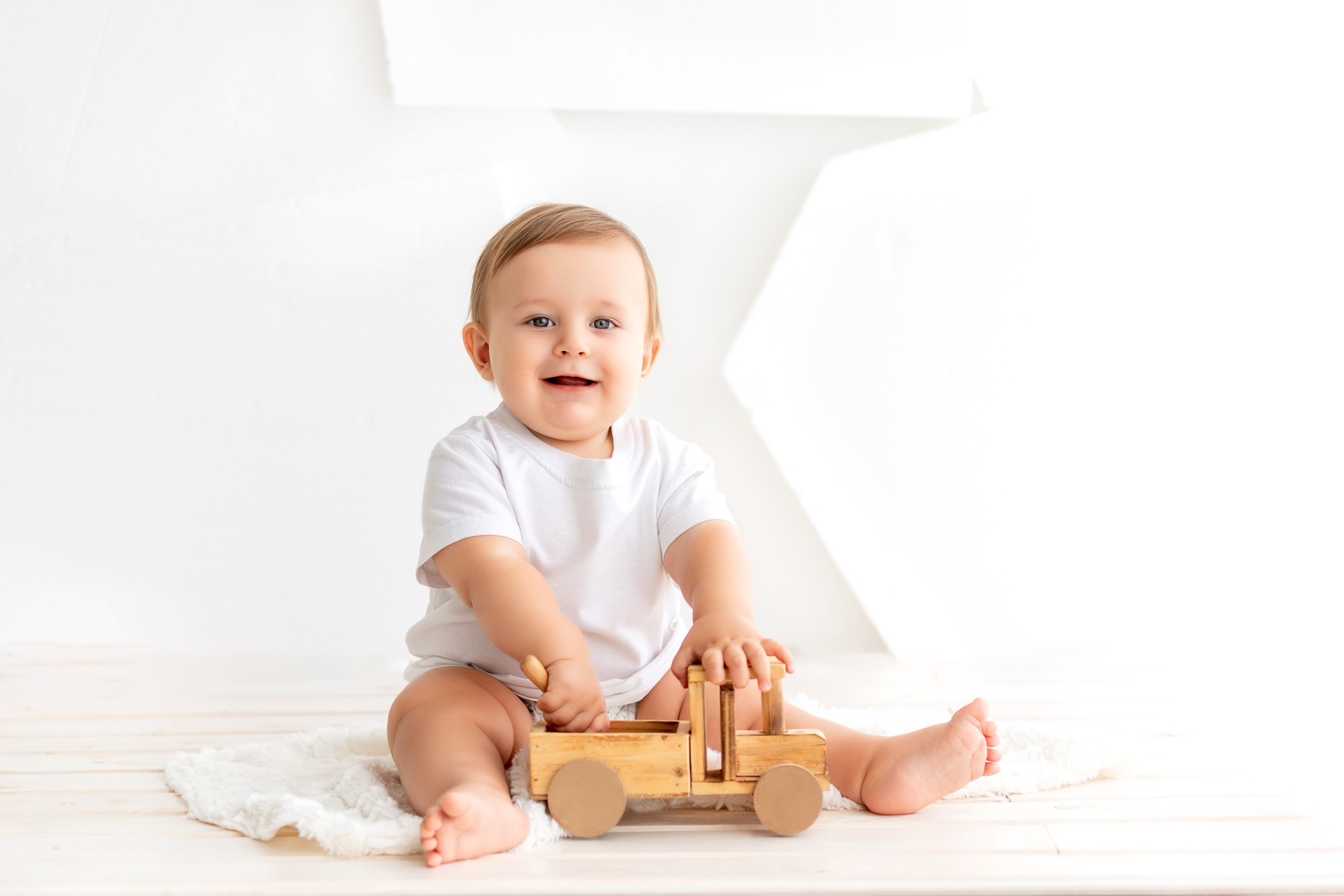 Sitzendes Baby von etwa sechs Monaten spielt mit einem Holzauto
